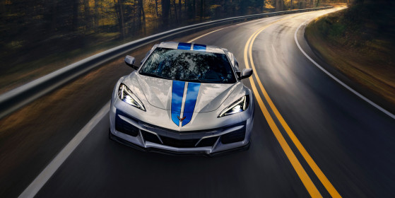 Front view of 2024 Chevrolet Corvette E-Ray 3LZ convertible in Silver Flare with Electric Blue stripe package driving on a road between trees. Pre-production model shown. Actual production model may vary. Model year 2024 Corvette E-Ray available 2023.