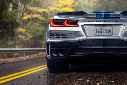 Close-up rear-view of 2024 Chevrolet Corvette E-Ray 3LZ convertible in Silver Flare with Electric Blue stripe package parked on a road in front of trees. Pre-production model shown. Actual production model may vary. Model year 2024 Corvette E-Ray available 2023.