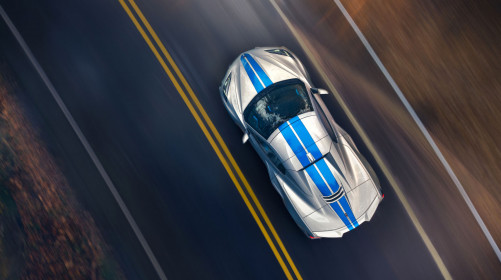 Overhead view of 2024 Chevrolet Corvette E-Ray 3LZ convertible in Silver Flare with Electric Blue stripe package driving on a road. Pre-production model shown. Actual production model may vary. Model year 2024 Corvette E-Ray available 2023.